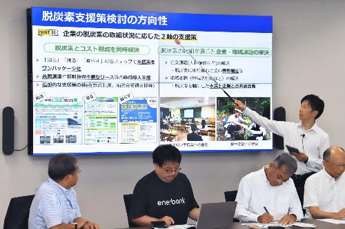モニターに映した脱炭素経営支援事業の説明資料を支持棒で指して市長が説明している