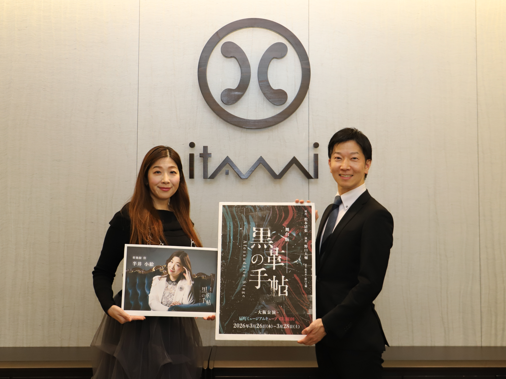 市長室の市章の前で舞台「黒川の手帖」のパネルをもってポーズをとる半井小絵さんと伊丹市長