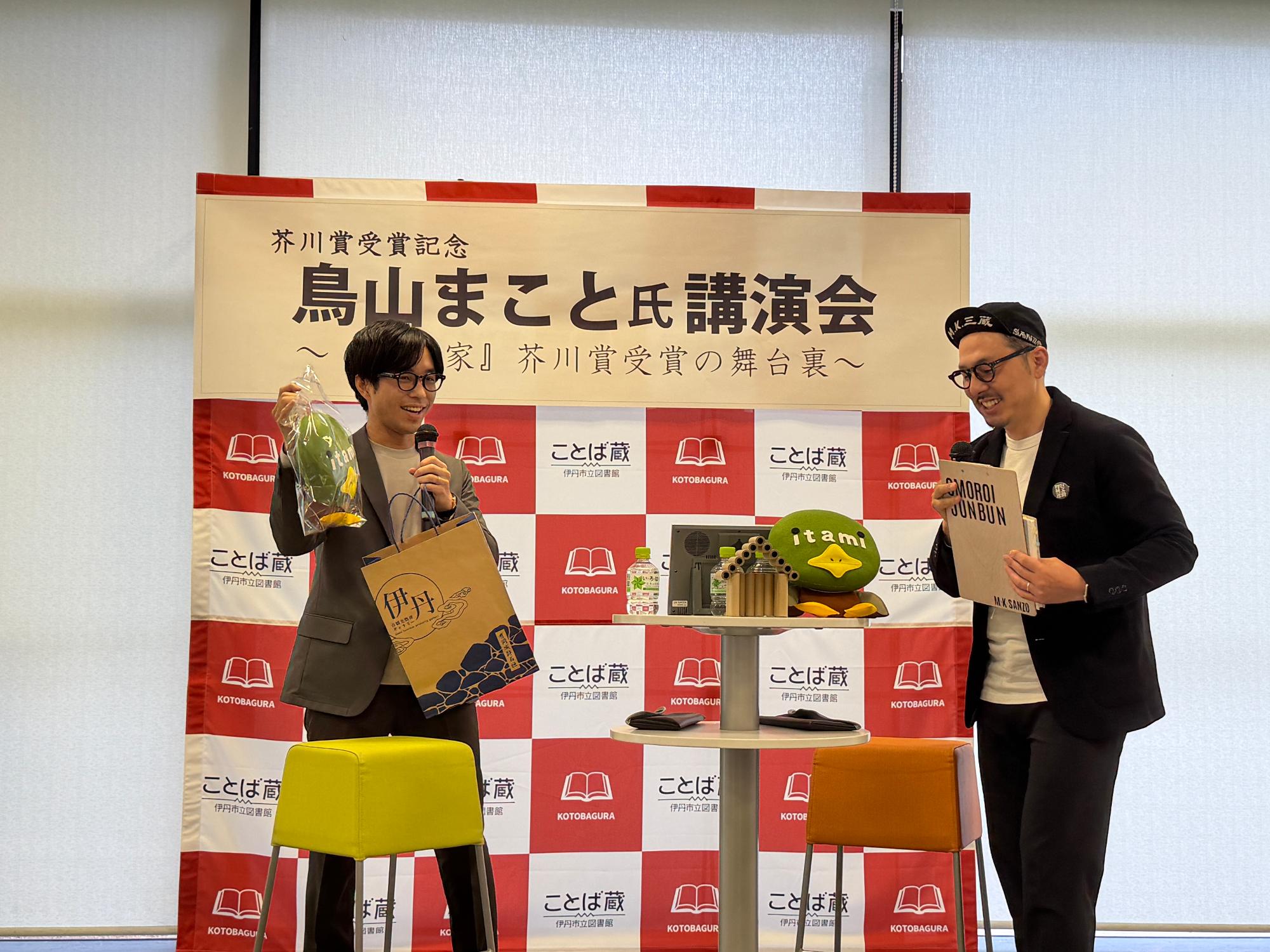 鳥山さんが松山さんから「たみまる」のぬいぐるみを受け取っている