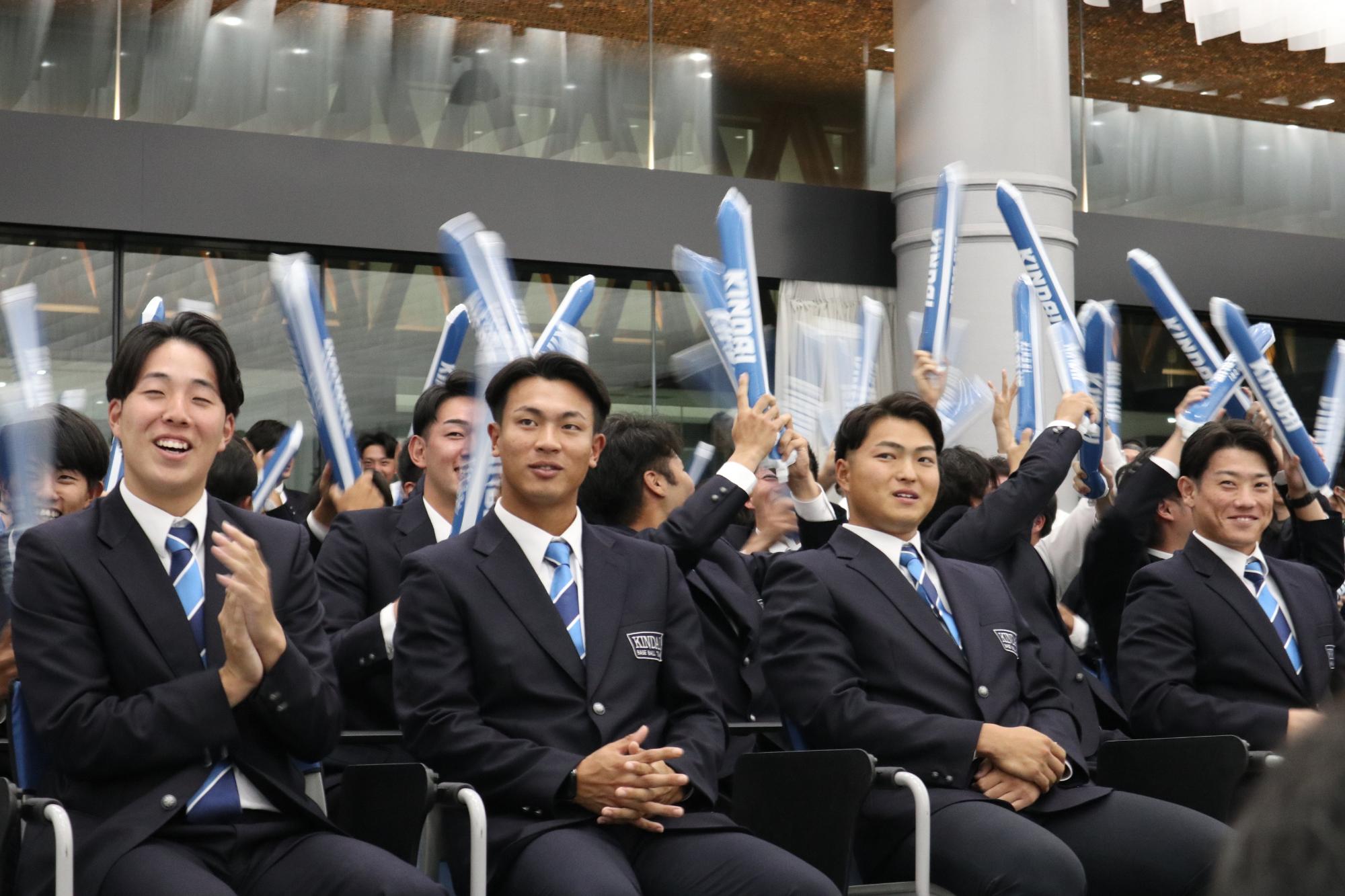 阪上選手のドラフト指名を受けて拍手が飛び交う近畿大学のホールの様子