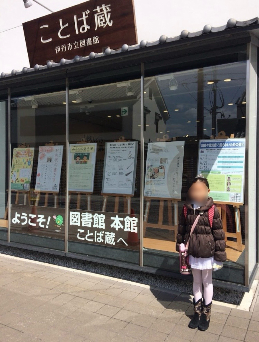としょかんことばぐらのいりぐちでしゃしんをとるおんなのこ